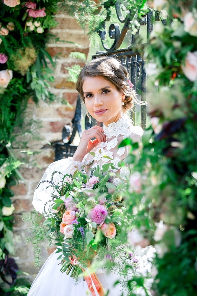 Bride wearing lace dress holding bouquet and surrounded by flowers, styled by Hair and Makeup by Gabrielle