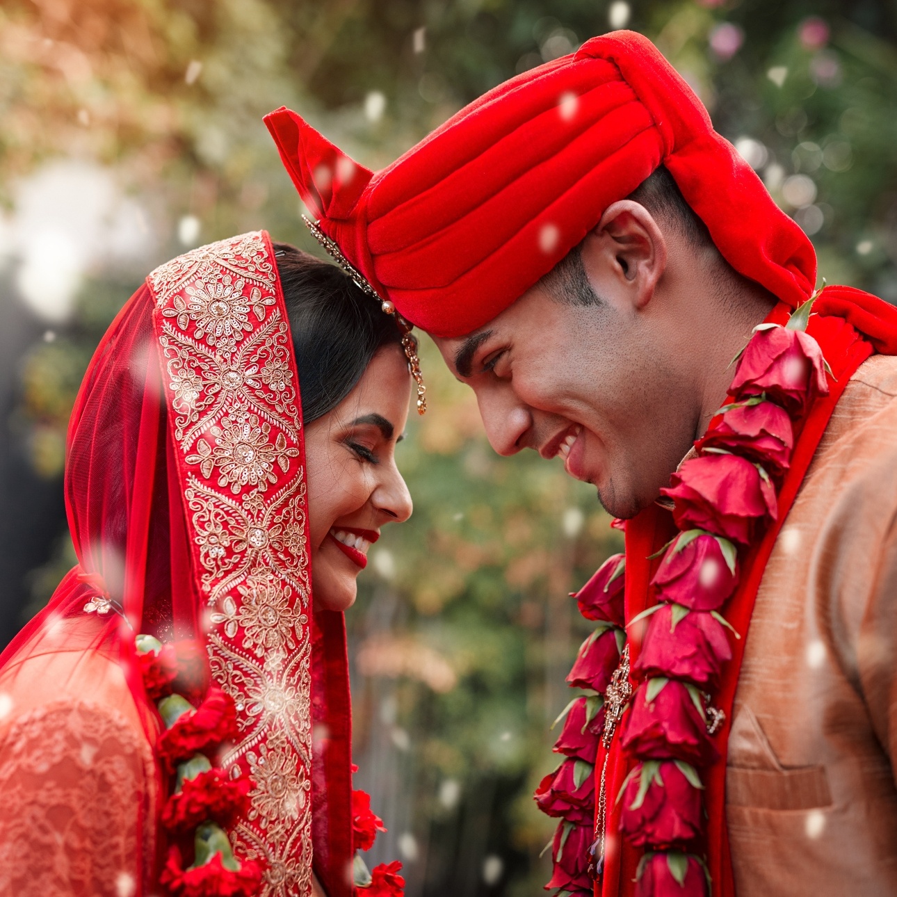 indian bride and groom on their wedding day in gold and red attire touching heads