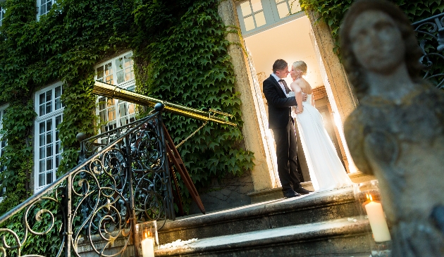couple in wedding clothes standing on the steps of a manor house covered in ivy