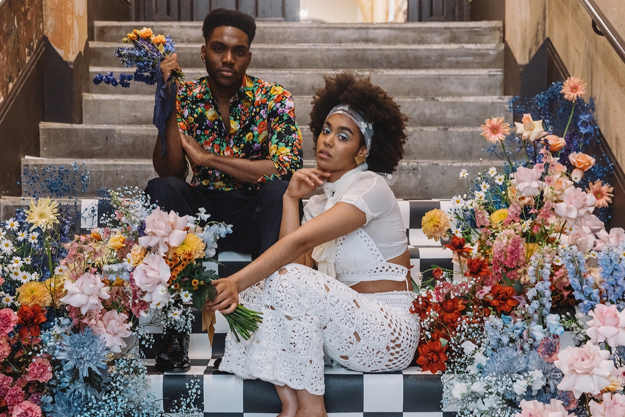 couple sitting on some steps in boho wedding gear surrounded by flowers