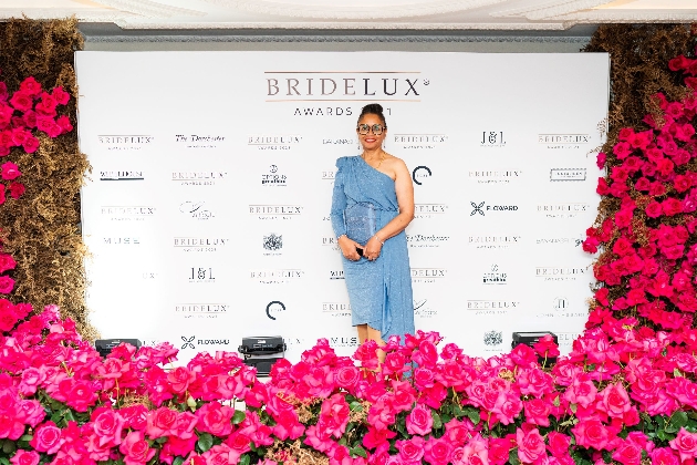 woman standing in a blue dress in front of a promotional wall