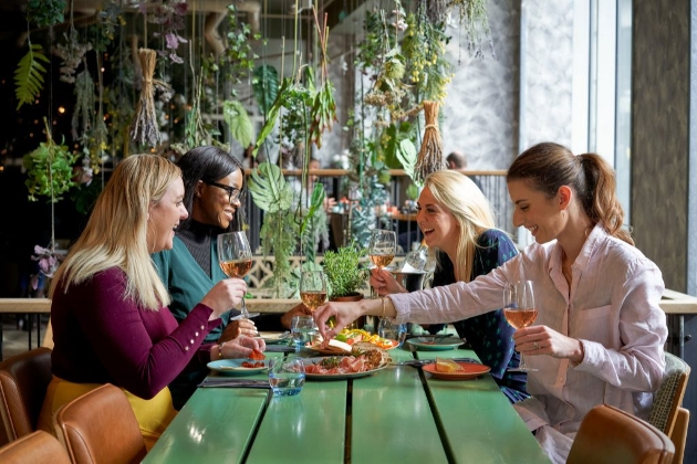 four women sat at a table with flowers hanging from the ceiling