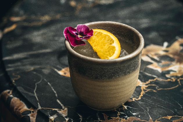 ceramic style cup with fluid inside and a slice of orange and a pansie on top