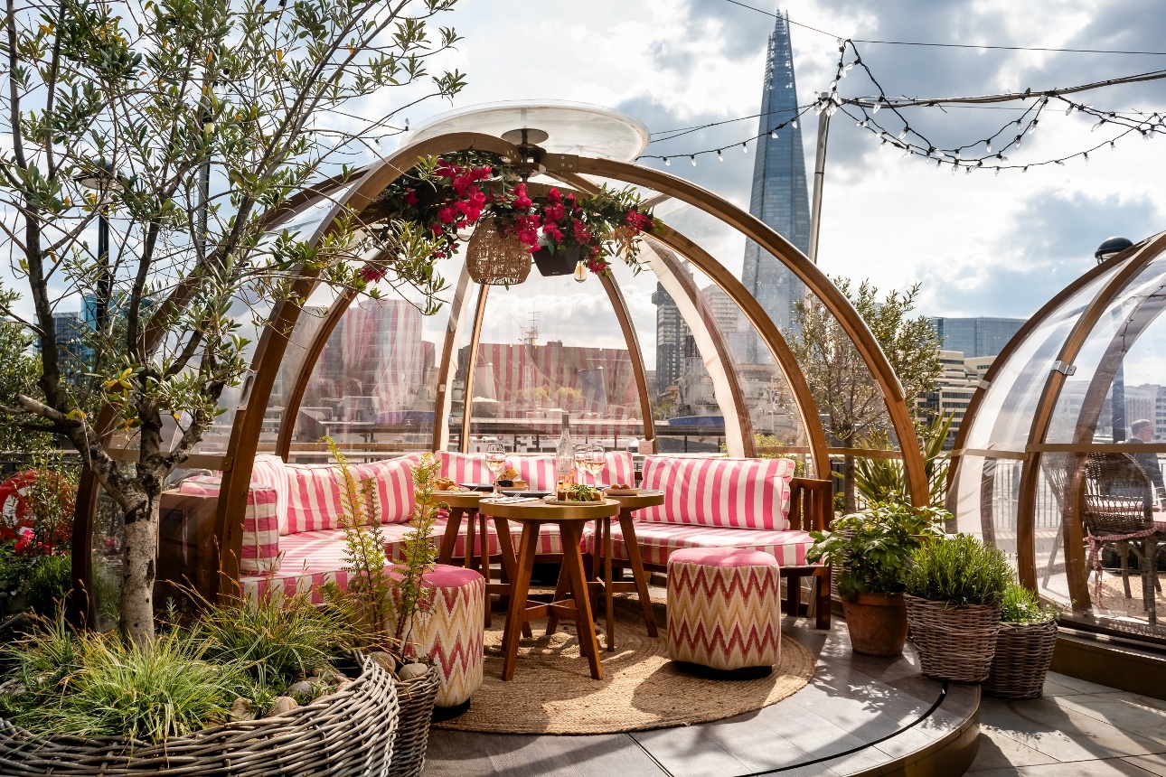 glass and wood dome with pink and white cushions, pod covered in flowers with london skyline in view
