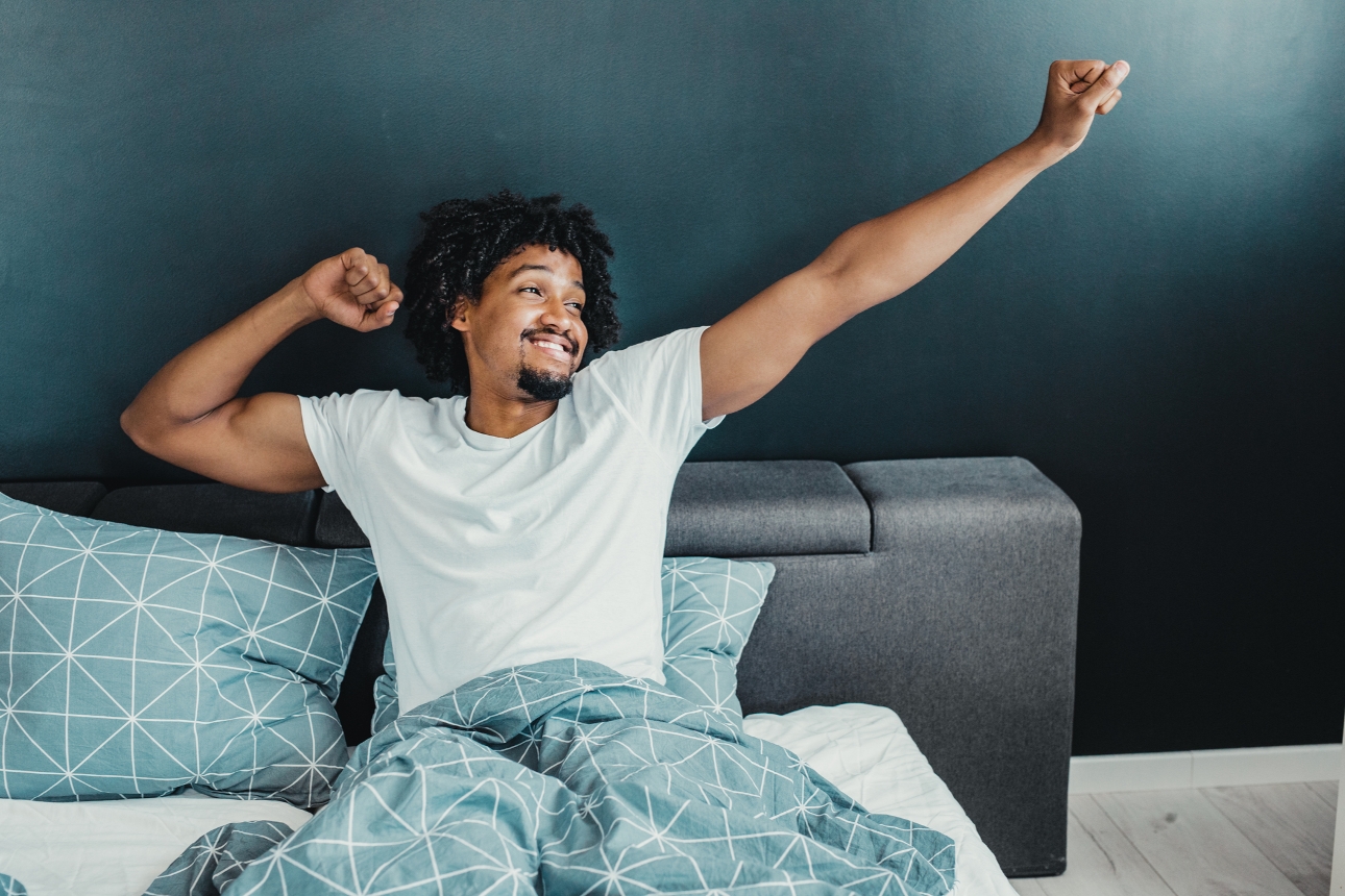 man waking up from a good nights sleep in a grey bed against blue walls
