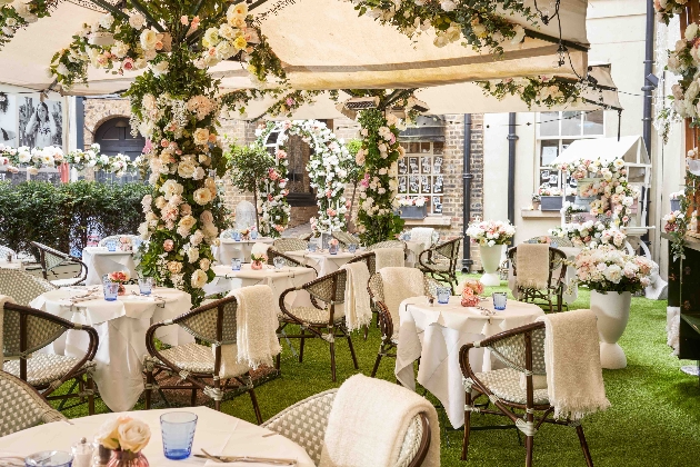 wicker tables and chairs at tables with clothes on and a marquee roof covered in flowers