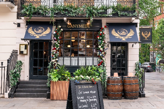 cream and black pub frontage with canopy, black and gold logos, lots of foliage