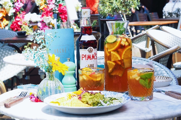 A bottle of pimms, with jug of pimms and glasses of pimms on a table with a salad