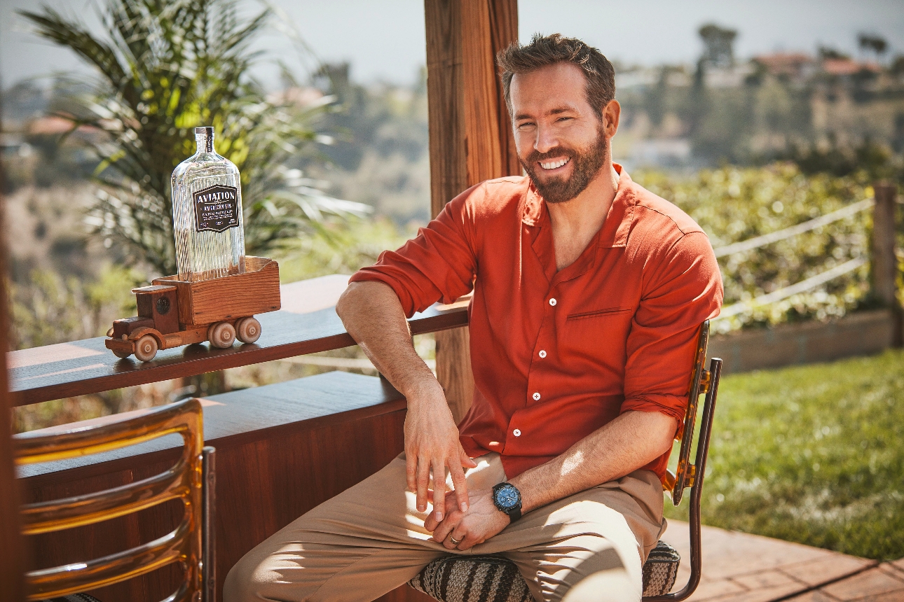 Ryan Reynolds sat by a pool bar with a bottle of gin on the counter