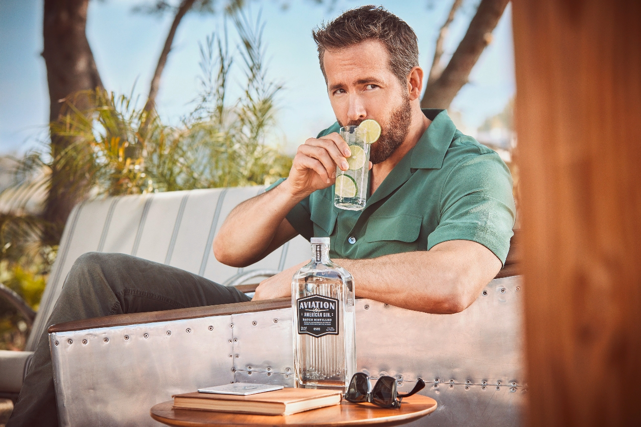 Ryan Reynolds sat on a pool sofa drinking a cocktail