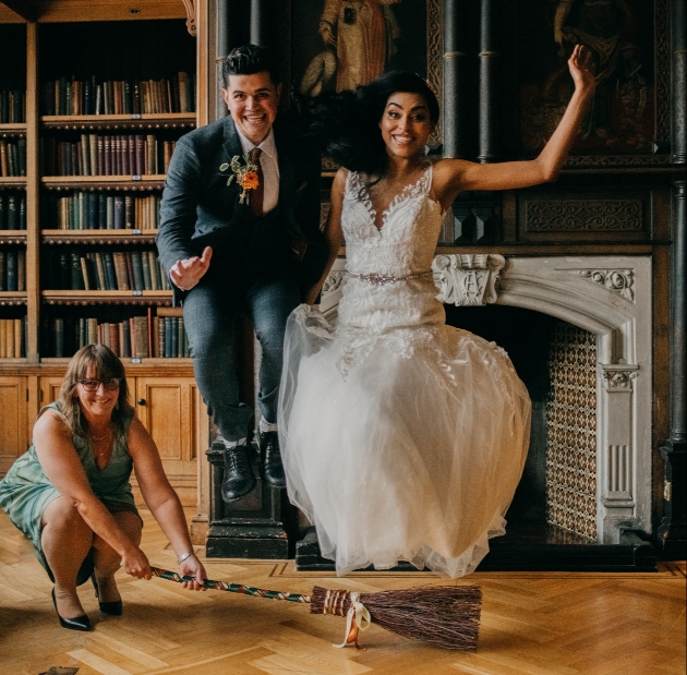 Amanda on floor with broom and bride and groom jumping over it