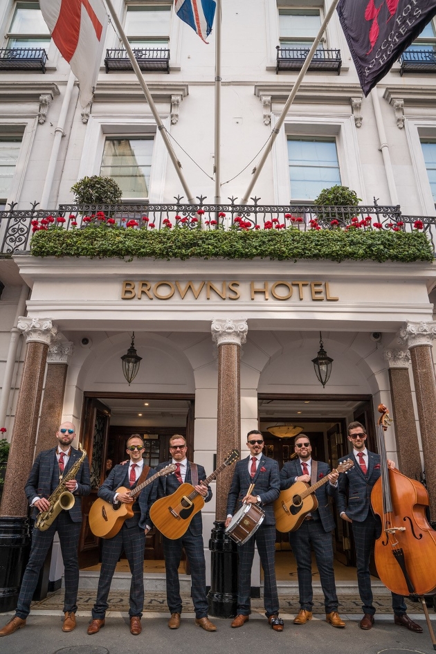 group of men suited holding guitars outside london hotel