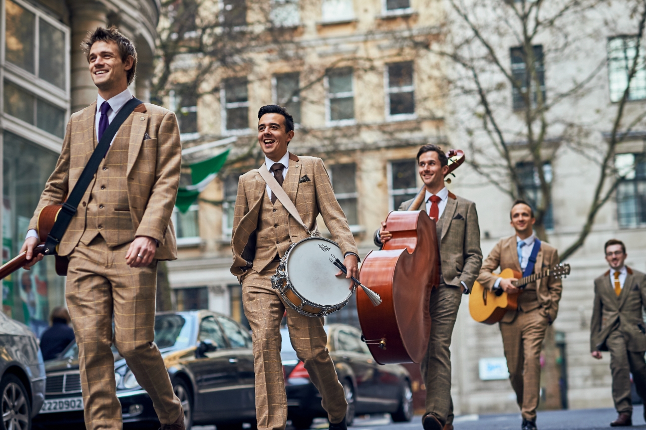 band in tweed suits holding instruments walking through London