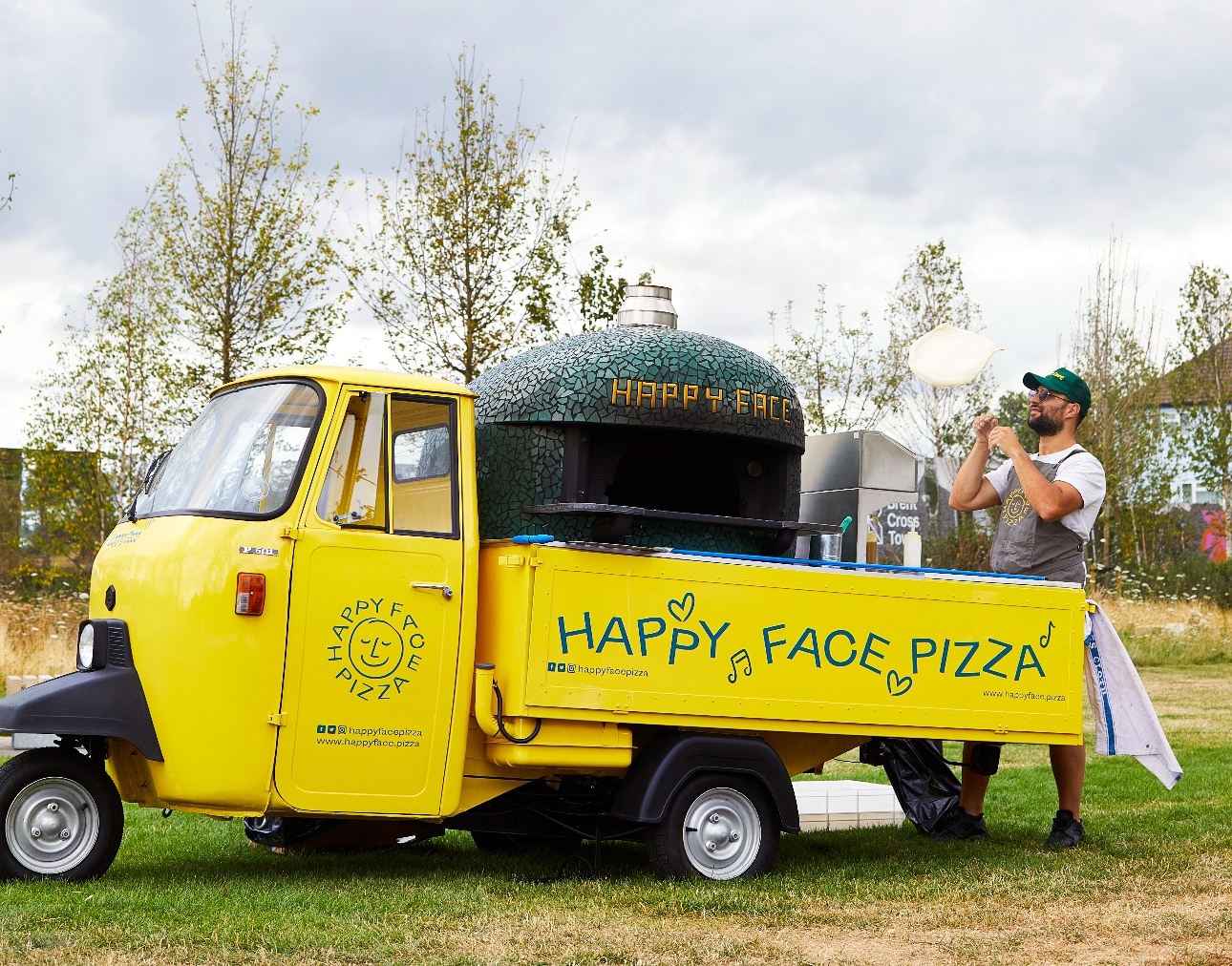 man tossing a pizza base in the air next to a pizza truck bright yellow in colour