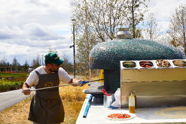 chef putting pizza in a pizza oven on back of a truck