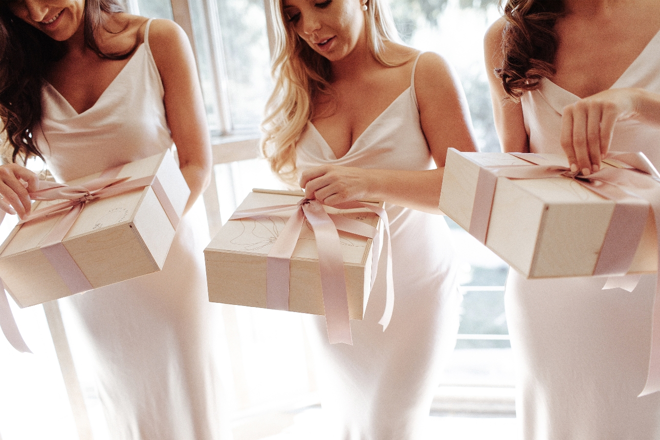 three women in white silk dresses opening boxes