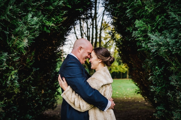 couple embracing in front of hedge bride in fur jacket