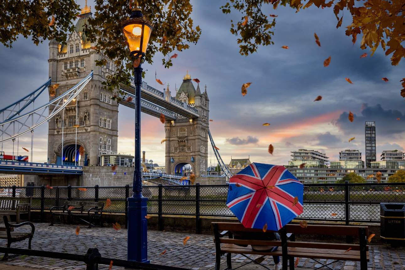 london bridge couple sat on bench near river under union jack umbrella