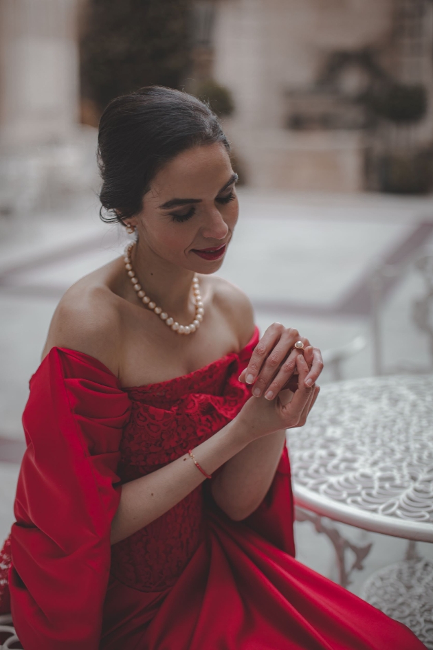 model in a red dress holding her pearl necklace