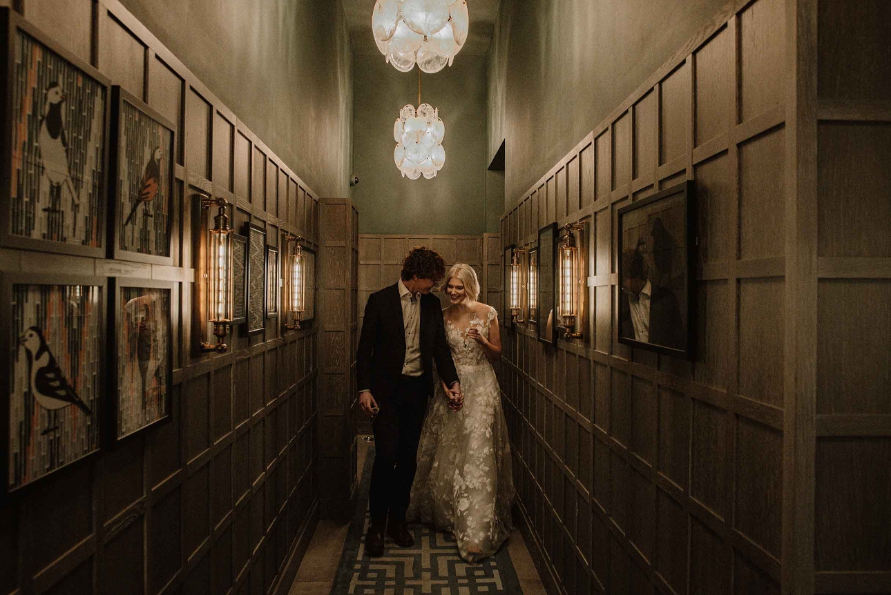 bride and groom walking along corridor with wood panelling and artwork on the walls