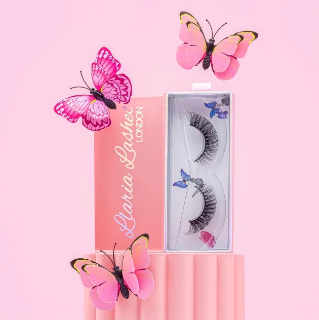 pack of faux lashes on a stand with pink background and butterflies around it