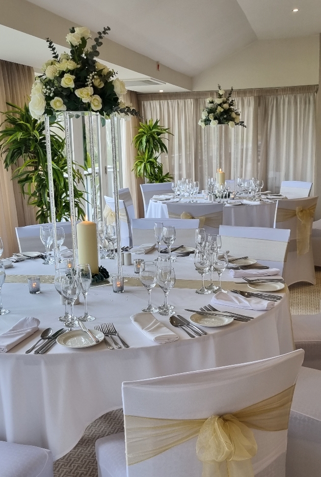 wedding breakfast table set up with white linen and green sash flowers for centrepiece