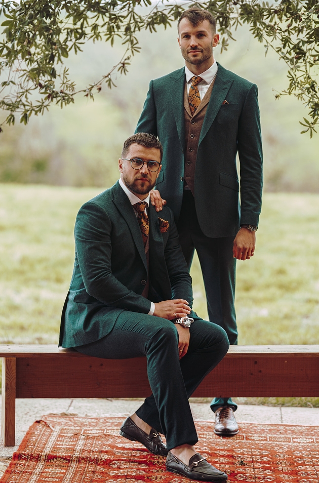 two models in green suits one sat down on a chair