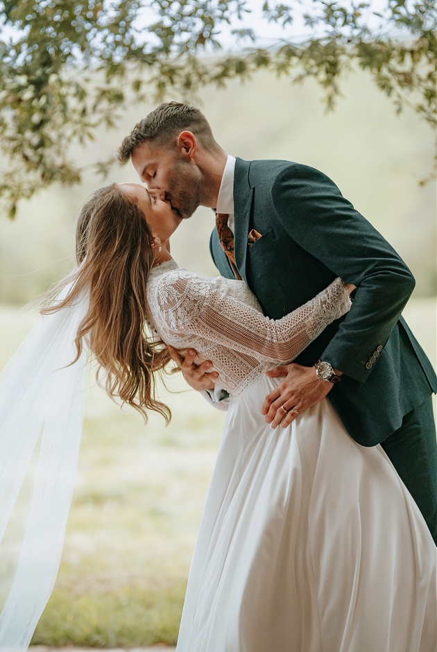 groom in green suit kissing bride while leaning her over
