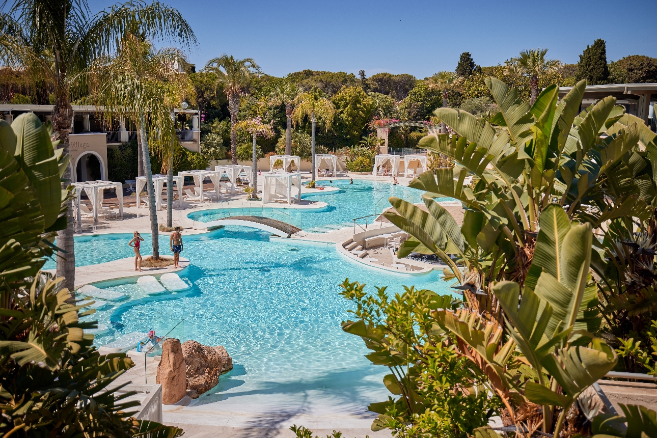 pool area lots of nooks seating in water, loungers on side, tropical plants and trees all around