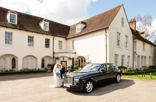 white manor house with bride and groom standing outside in front of wedding car